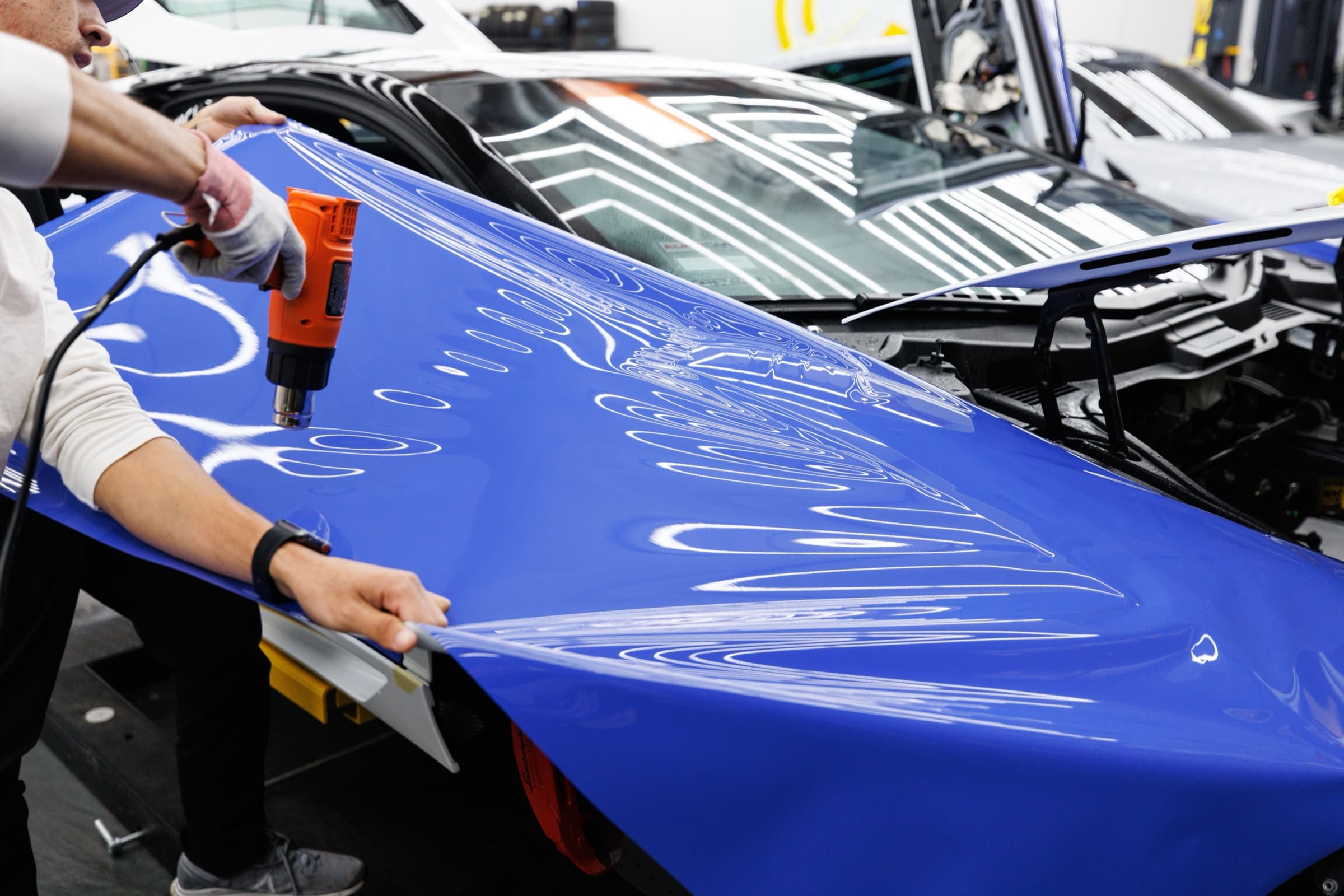 Folierer bringen mit Heißluft und Rakel eine blaue Folie auf eine Motorhaube auf